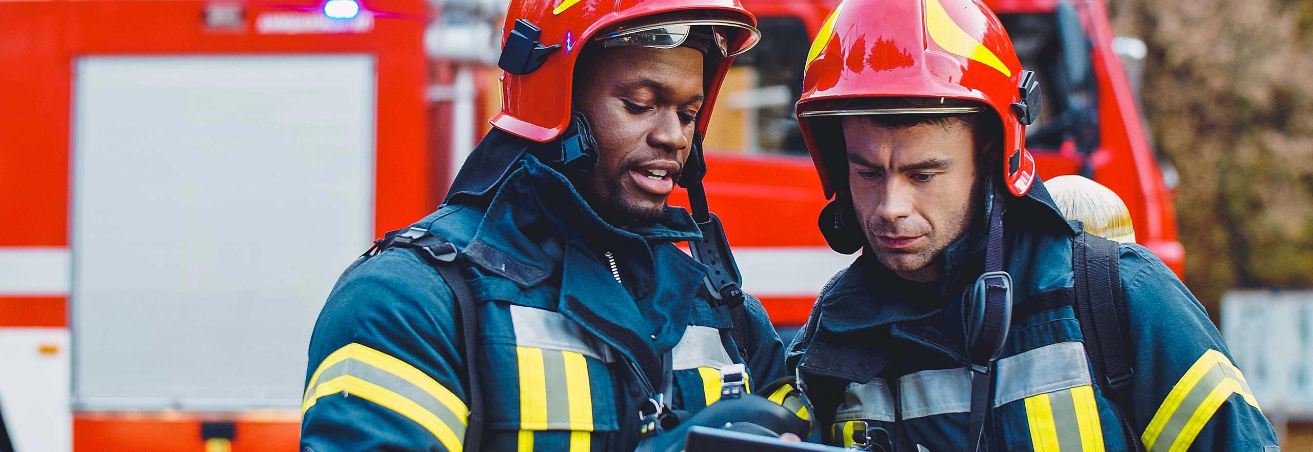 Portrait of two firefighters in fire fighting operation, fireman in protective clothing and helmet using tablet computer in action fighting.